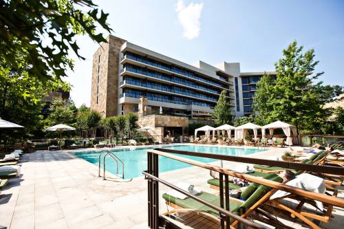A sunny hotel pool area with lounge chairs, umbrellas, and a modern building in the background.