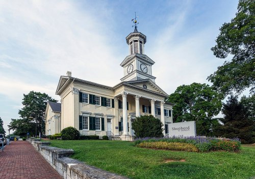 Historic building with a clock tower, surrounded by greenery and a sign that reads "Shepherd." Clear blue sky above.