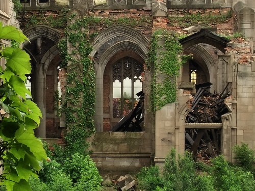 Ruins of a stone building with ivy-covered walls and a collapsed interior, surrounded by greenery.