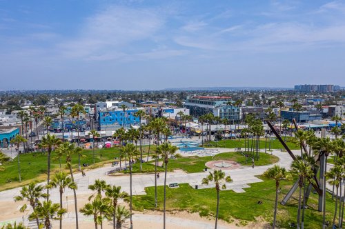 Aerial view of a vibrant coastal area with palm trees, a park, and colorful buildings in the background under a clear sky.