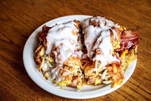 A plate of crispy fried food topped with bacon and a creamy white sauce, served on a wooden table.