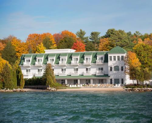A white hotel with green roofs by a lake, surrounded by colorful autumn trees and a clear blue sky.