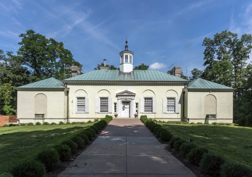 A light green building with a central entrance, a cupola, and landscaped grounds under a blue sky.