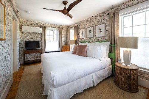 Cozy bedroom with floral wallpaper, two beds, a TV, and stylish decor, featuring a ceiling fan and natural light.