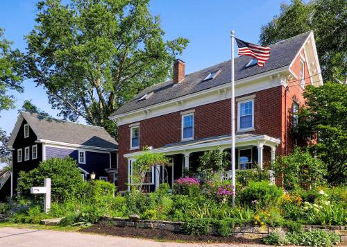 A charming brick house with a flag, surrounded by colorful flowers and greenery on a sunny day.