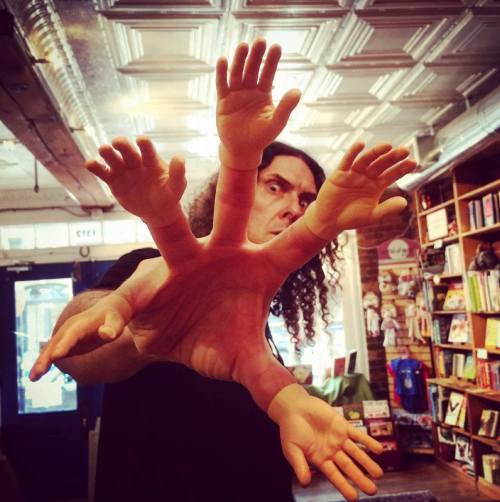 A person with curly hair holds out a hand with multiple toy hands attached, creating a whimsical effect.