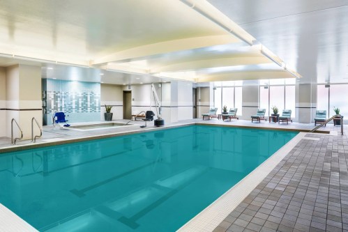 Indoor swimming pool with clear blue water, lounge chairs, and modern decor. Brightly lit with large windows.