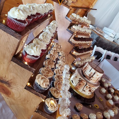 A dessert display featuring various cupcakes and a multi-tiered cake on a wooden stand, decorated with lights.
