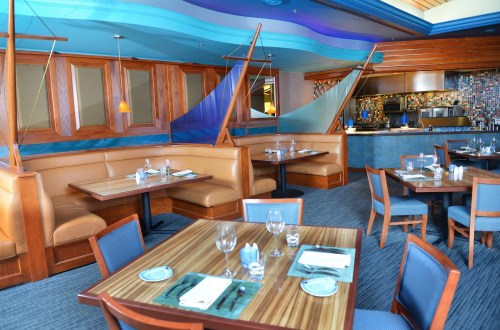 Interior of a modern restaurant featuring wooden booths, blue accents, and a colorful tiled bar area.