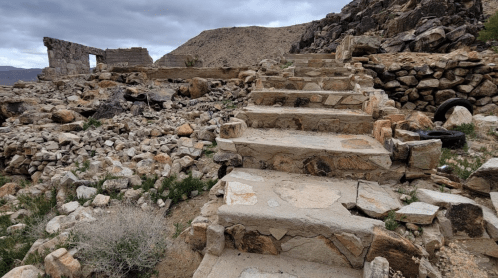 Stone steps lead through rocky terrain to the ruins of a structure under a cloudy sky.