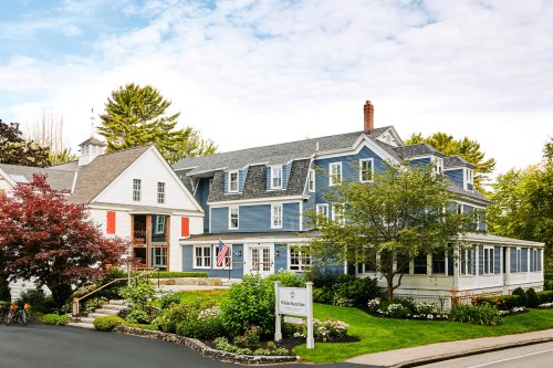 A charming blue house with a porch, surrounded by greenery and a sign for "White Barn Inn."