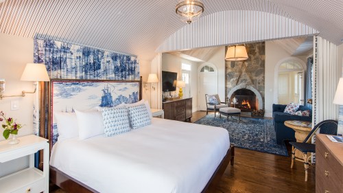 Cozy bedroom with a fireplace, blue and white decor, and a sitting area, featuring elegant lighting and wooden floors.