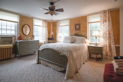 Cozy bedroom with a bed, dresser, and warm lighting from lamps and windows, featuring a vintage decor style.