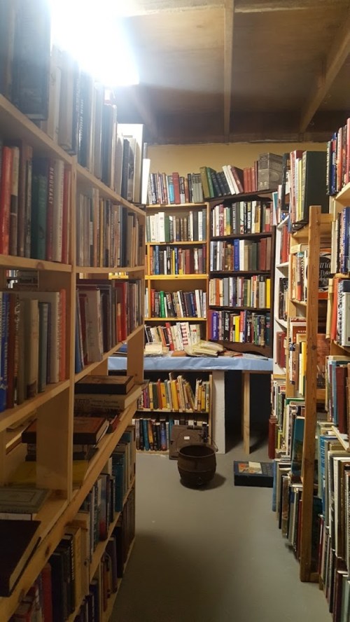 A cozy, narrow room filled with tall bookshelves packed with books, creating a warm, inviting reading space.