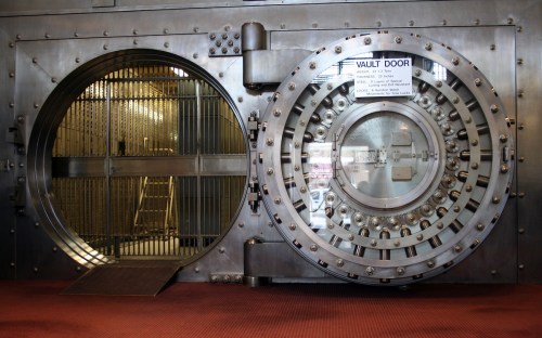 A large, metallic vault door with a circular design, partially open, revealing a secure interior.