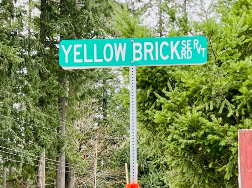 Street sign for "Yellow Brick Road" surrounded by tall green trees.