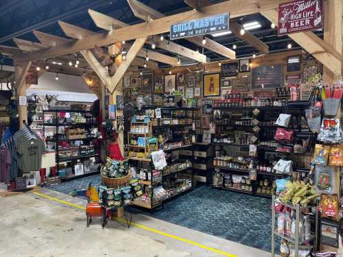 A cozy shop display featuring grilling supplies, snacks, and beer, with wooden beams and various merchandise on shelves.