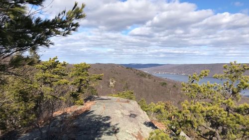A scenic view from a rocky outcrop, overlooking a valley with trees and a river under a partly cloudy sky.