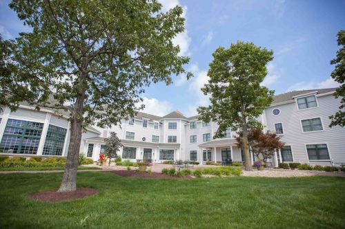 A well-maintained building surrounded by green grass, trees, and colorful landscaping under a blue sky.