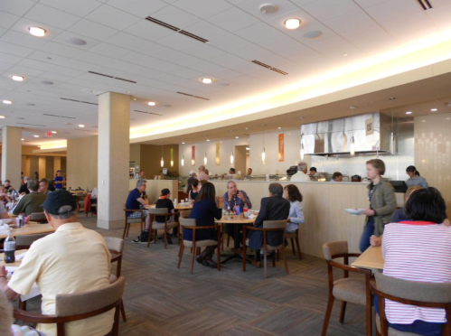 A busy dining area with people seated at tables, a serving counter in the background, and a warm, inviting atmosphere.