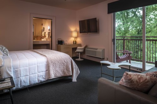 A cozy hotel room featuring a bed, TV, seating area, and a balcony with a view of greenery outside.