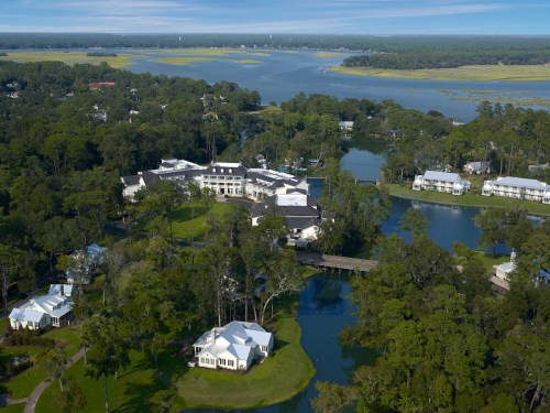 Aerial view of a resort surrounded by lush greenery and waterways, with a serene landscape in the background.