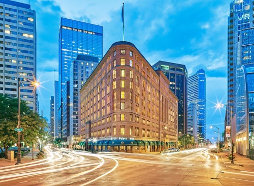 Historic building at dusk, surrounded by modern skyscrapers and light trails from passing cars.
