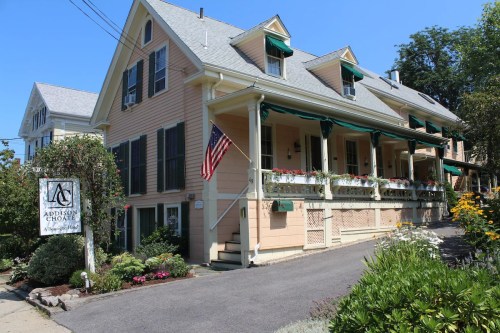 A charming pink house with green shutters, flower boxes, and an American flag, featuring a sign for Addison Choate.