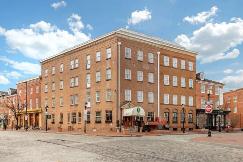 Historic brick building on a cobblestone street, featuring large windows and a welcoming entrance under a blue sky.