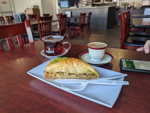 A plate with a pastry filled with meat, a cup of tea, and a small coffee on a table in a cozy café setting.