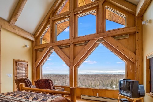 Cozy room with large wooden windows offering a scenic view of a forested landscape and blue sky.