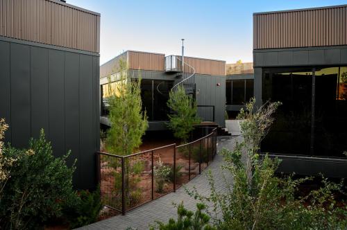 Modern buildings with dark exteriors surround a landscaped pathway and greenery, under a clear blue sky.
