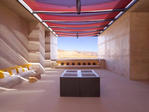 Modern interior with a minimalist design, featuring a central table and large windows showcasing a desert landscape.