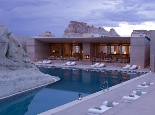 Modern resort with a serene pool, lounge chairs, and stunning mountain views under a cloudy sky.