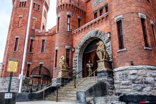 Historic brick building with towers, stone lion statues at the entrance, and a staircase leading up to the door.