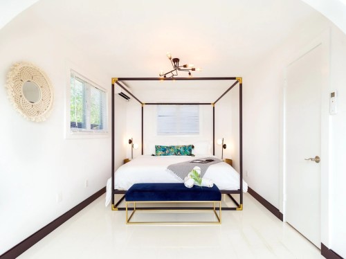 A modern bedroom featuring a four-poster bed, stylish lighting, and a blue bench at the foot of the bed.