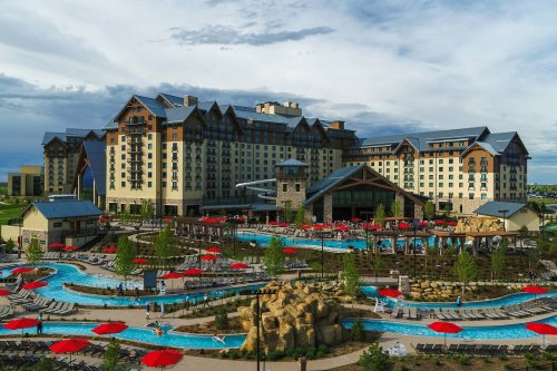 A large resort hotel with a pool area, surrounded by greenery and red umbrellas under a cloudy sky.