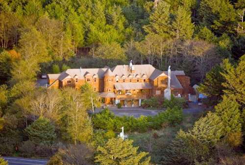 Aerial view of a large wooden lodge surrounded by dense green trees.