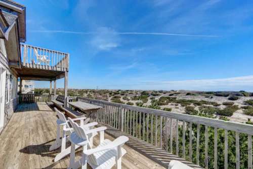 A wooden deck with white chairs overlooks a scenic landscape under a clear blue sky.