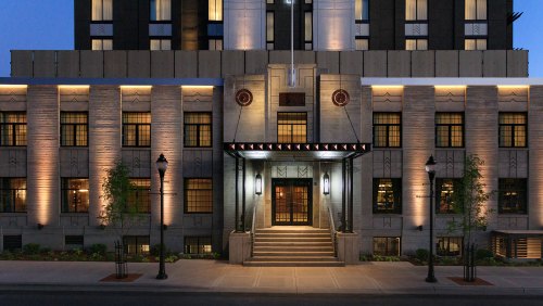 Art Deco-style hotel entrance with illuminated facade and steps, featuring large windows and decorative elements.