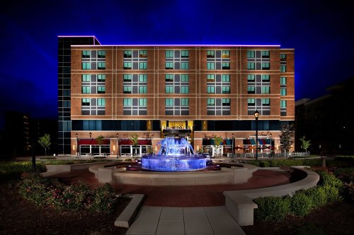 A modern hotel building illuminated at night, featuring a fountain in the foreground and vibrant blue lighting.