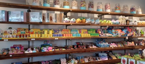A colorful candy shop display with jars of sweets, toys, and various treats on wooden shelves.