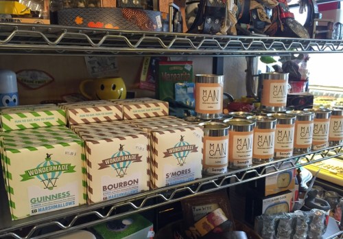 A shelf displaying various flavored marshmallows and candles, including Guinness, Bourbon, and S'mores.