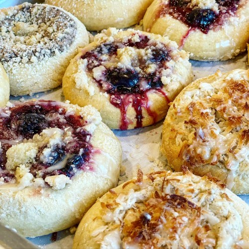A close-up of assorted pastries with fruit fillings and toppings, including crumbly and coconut variations.