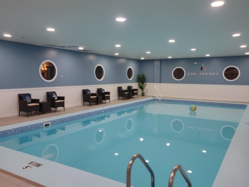 Indoor swimming pool with blue walls, circular windows, and seating area. A colorful beach ball floats in the water.