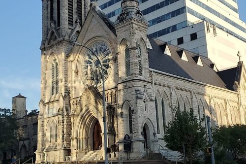 Historic stone church with a large rose window, set against a modern skyscraper in the background.