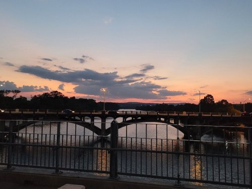 A sunset view over a bridge, with clouds reflecting on the water and a serene landscape in the background.