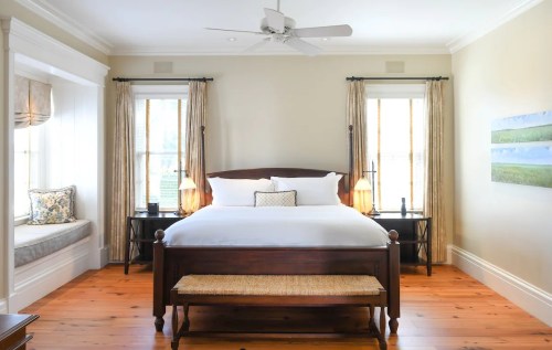 Bright, airy bedroom with a wooden bed, two nightstands, and a cozy window seat. Light curtains and wooden floors enhance warmth.