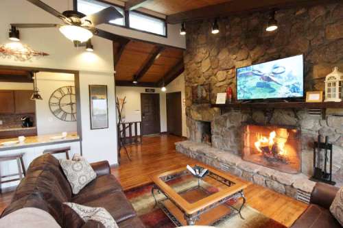Cozy living room with a stone fireplace, wooden beams, and a TV above the mantle, featuring a warm, inviting atmosphere.