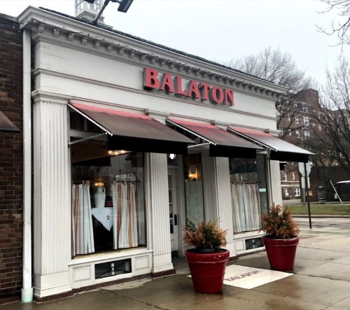 Exterior of Balaton restaurant featuring a red sign, awnings, and potted plants on a rainy day.